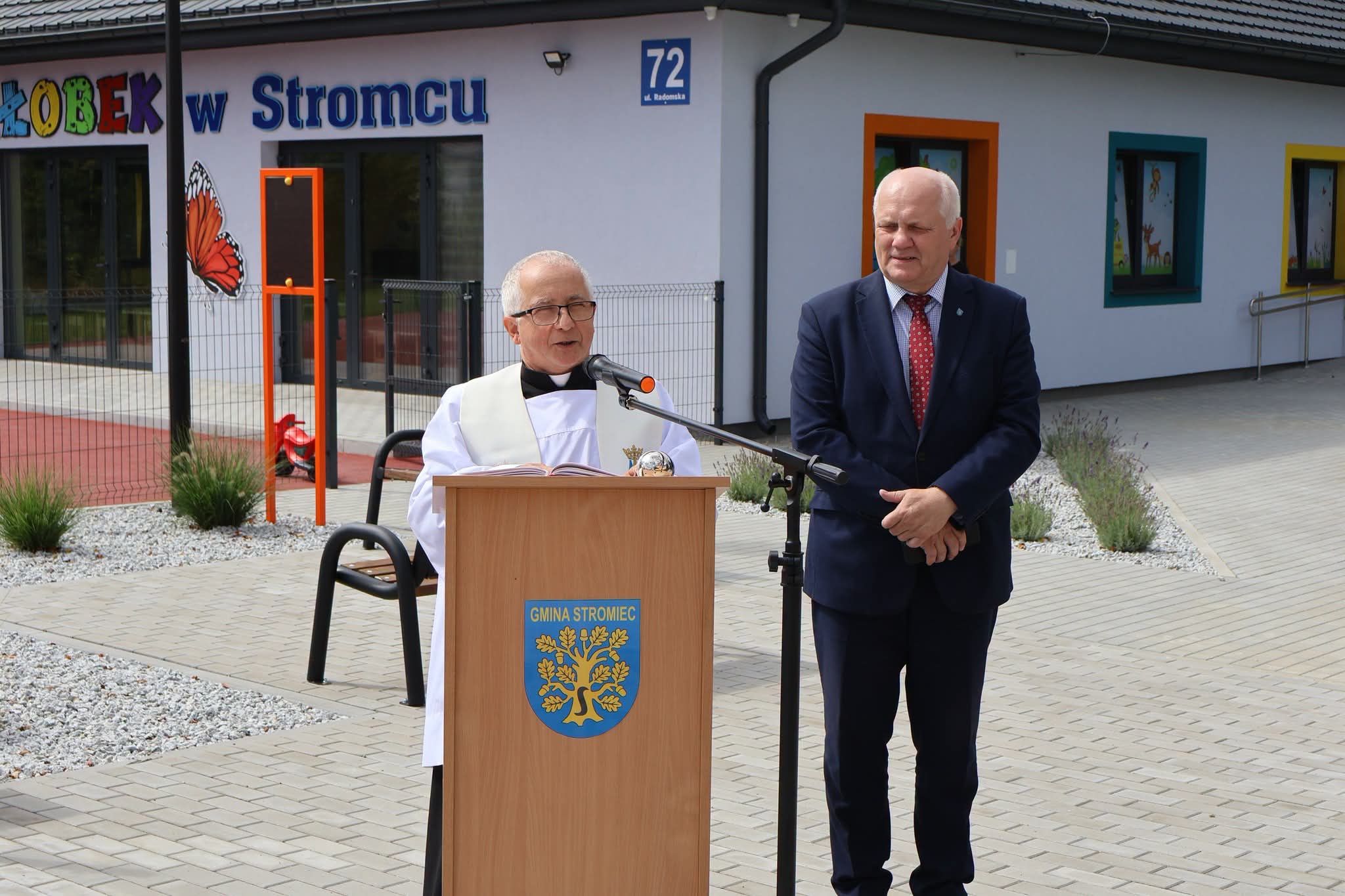 Modlitwa poświęcenia odczytywana przy mównicy z herbem Gminy Stromiec, przed budynkiem żłobka